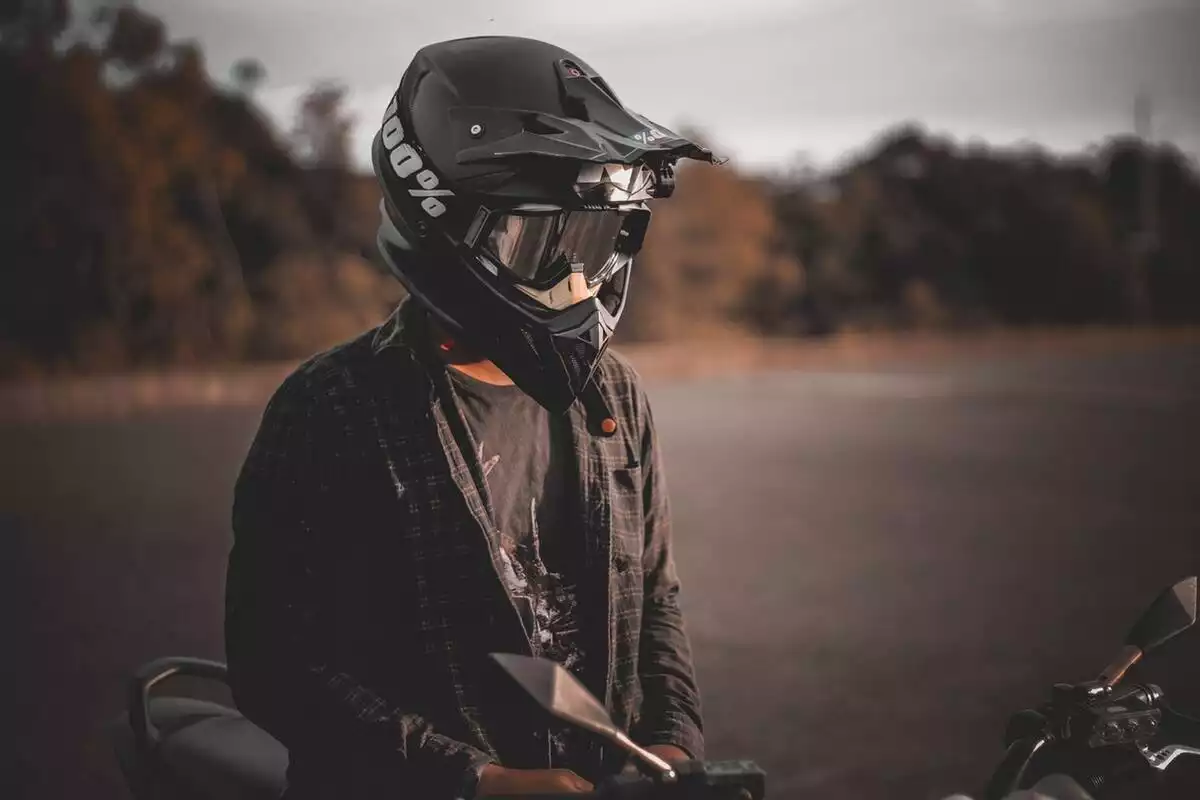 Chico con casco de motorista montado encima de su moto