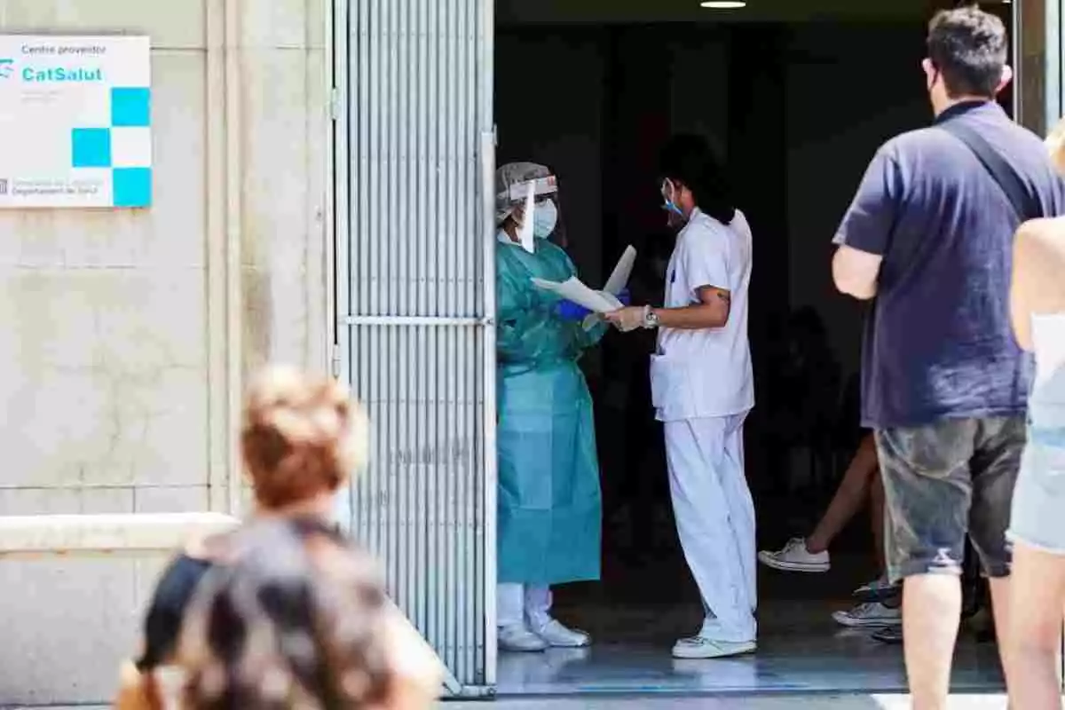 Sanitaris a les portes d'un hospital, amb mascaretes i equips protectors, mentre els pacients fan cua fora de l'edifici