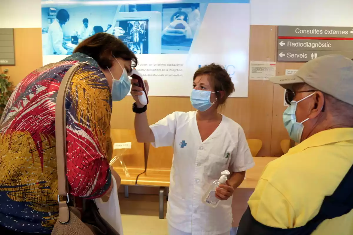 Una infermera prenent la temperatura a dos pacients abans que entrin a consultes externes de l'Hospital Verge de la Cinta de Tortosa