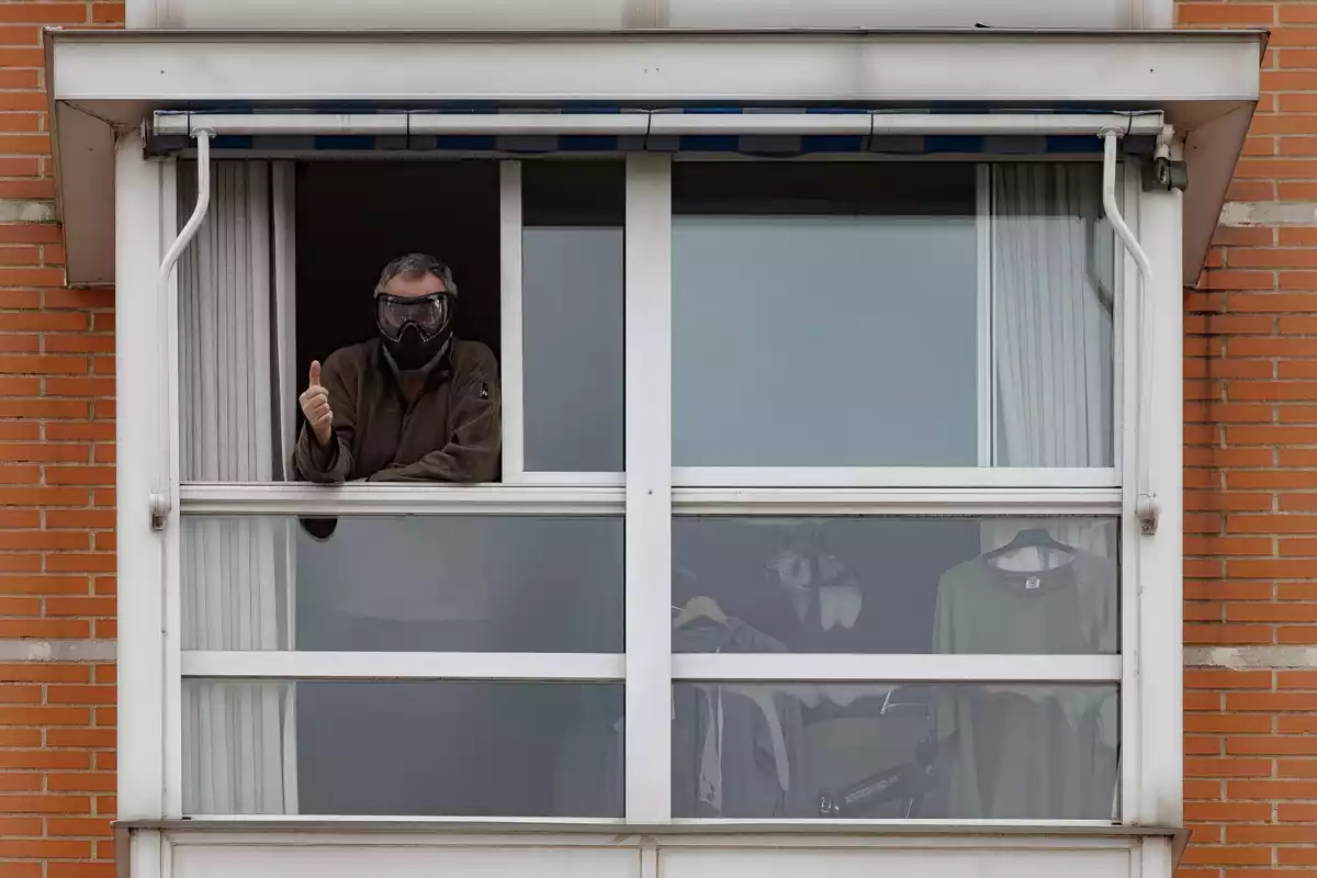 Un hombre con la cara protegida saluda desde su ventana en Madrid durante el confinamiento