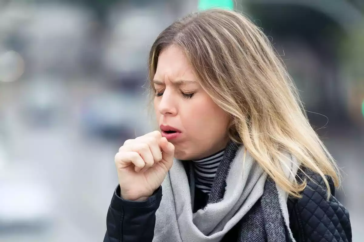 Chica rubia con la mano en la boca tras toser en la calle