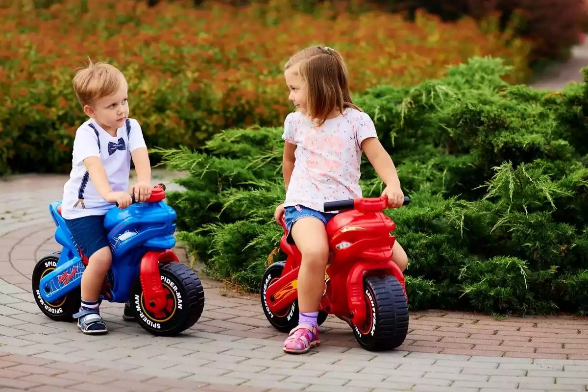 Foto de una niña y un niño subidos en una moto de juguete