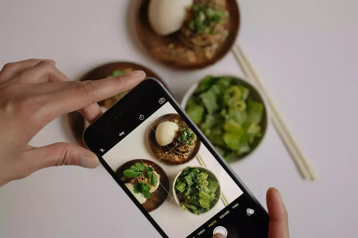 Unas manos haciendo una foto con un teléfono a unos platos con verduras
