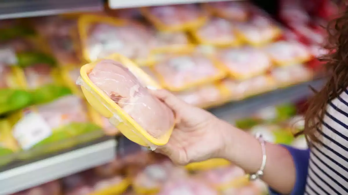 Fotografía de una mujer sujetando una bandeja de pollo en el supermercado