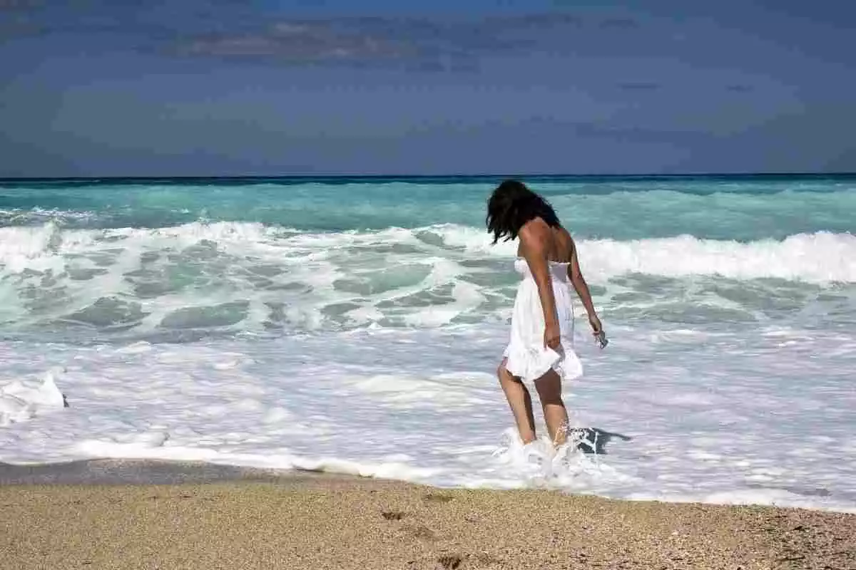 Mujer paseando en una playa con oleaje