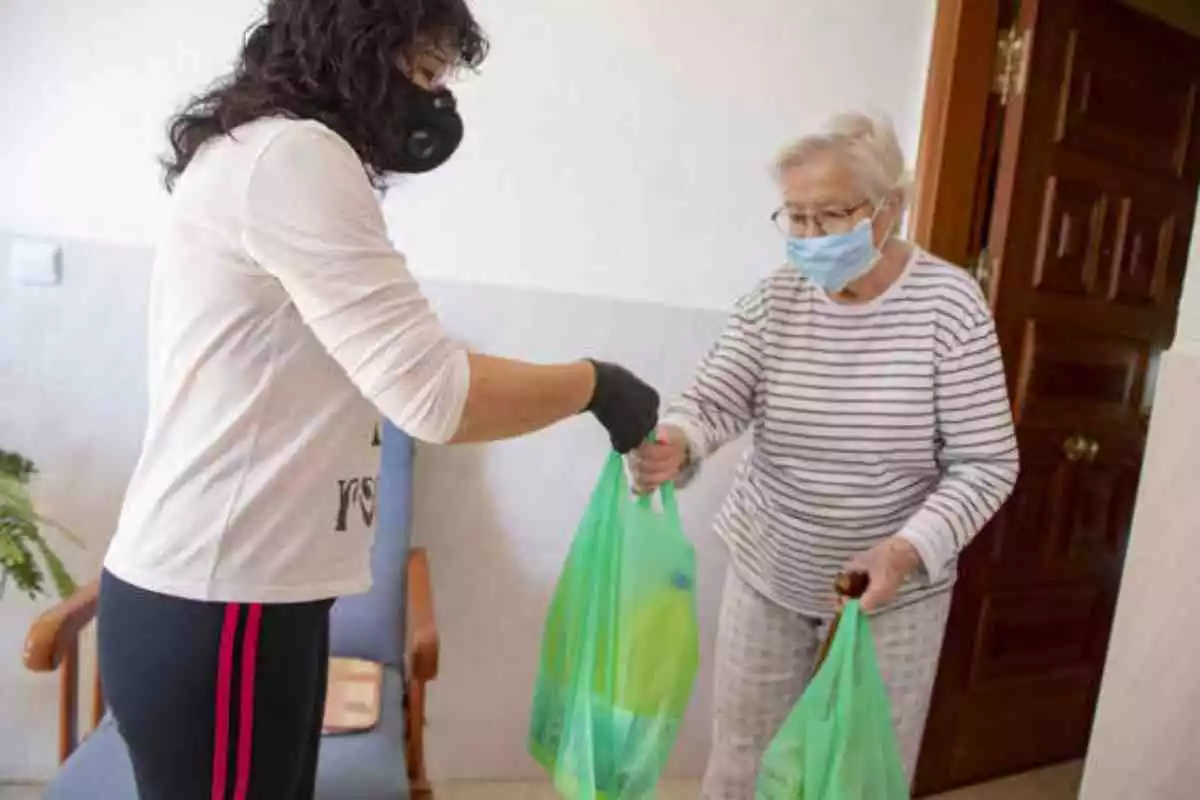 Una voluntara llevando la compra a una anciana durante la crisis del Coronavirus