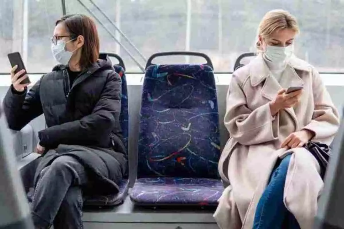 Pasajeras utilizando el teléfono móvil durante un trayecto en autobús con mascarillas de protección