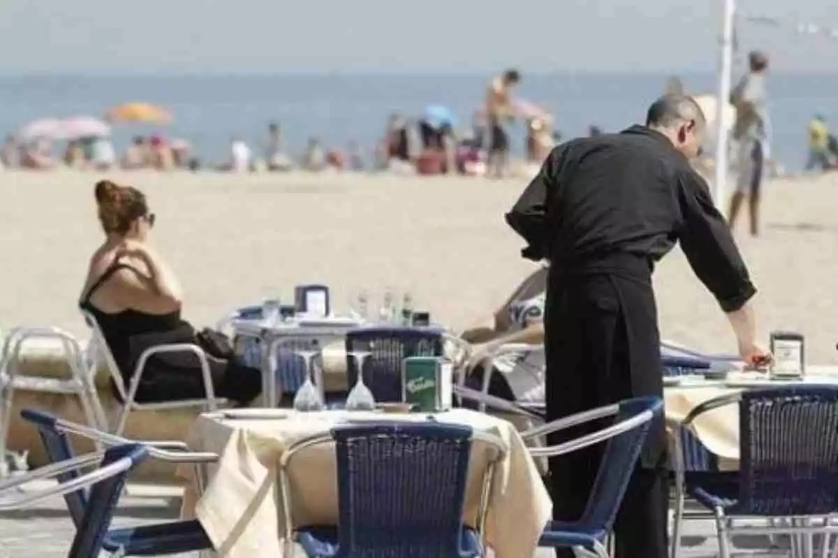 Un camarero sirviendo en unas mesas en la playa durante el verano