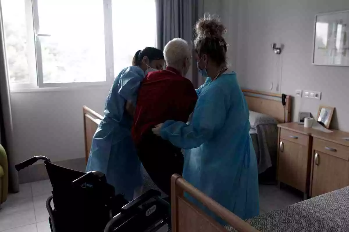 Enfermeras ayudan a un residente anciano a sentarse en una silla de ruedas en Madrid
