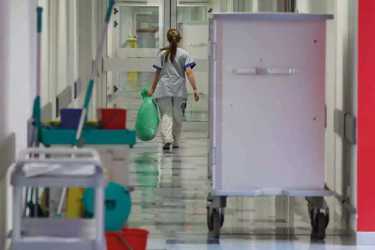 Una limpiadora se aleja a lo lejos en un pasillo de un hospital con una bolsa en la mano