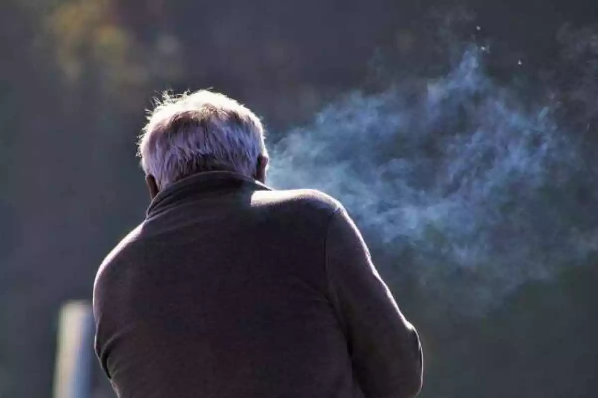 Imagen de un hombre fumando de espaldas expulsando el humo