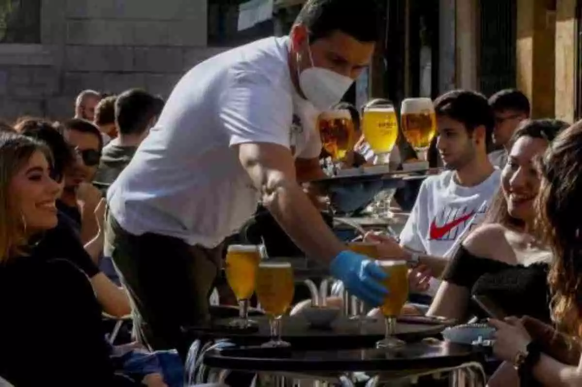 Camarero con mascarilla sirve unas cervezas a unas clientas en una terraza
