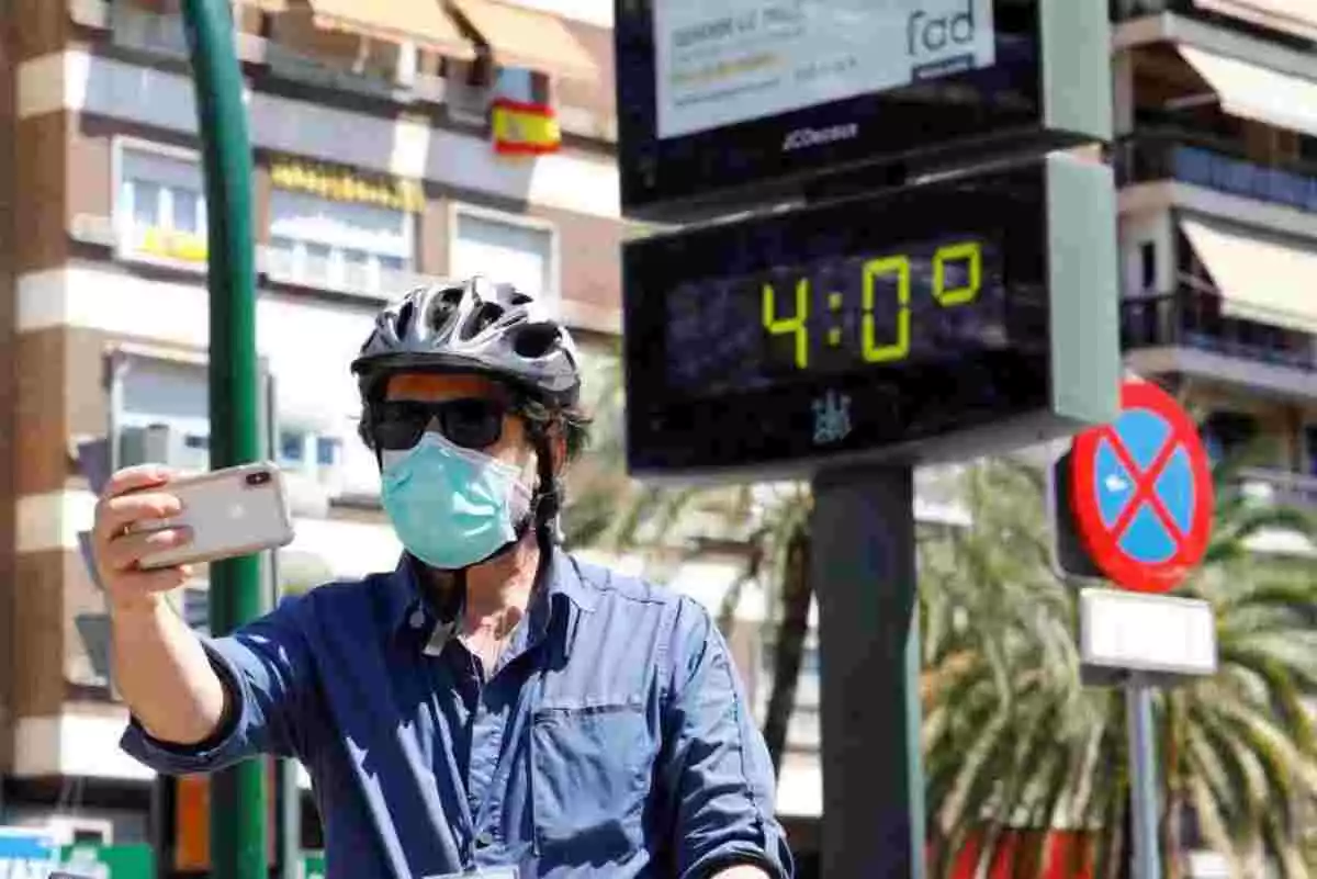 Imagen de un hombre con mascarilla frente a un termómetro que marca 40ºC