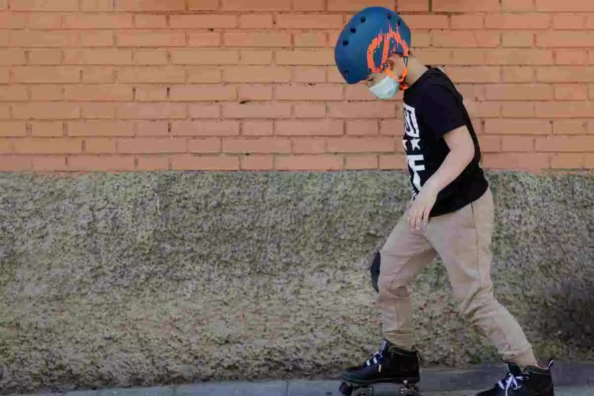 Un niño patina por la calle protegido con una mascarilla