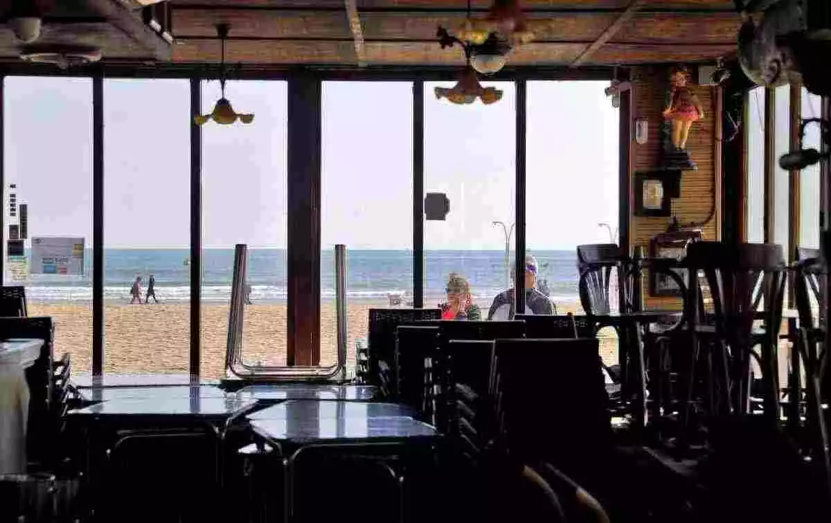 Dos personas observan el interior de un restaurante de la playa de La Malvarrosa de Valencia cerrado.