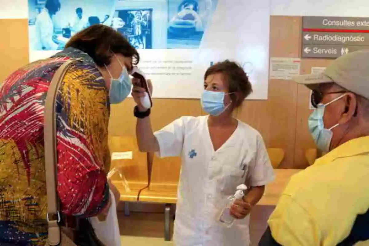 Una sanitaria tomando la temperatura a dos personas en un centro sanitario en Cataluña