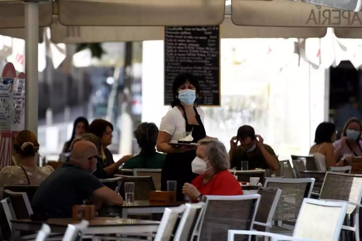 Una camarera con mascarilla atiende a los clientes en una terraza de un bar el día en el que entra en vigor en la Comunidad de Madrid la ampliación del uso obligatorio de la mascarilla,