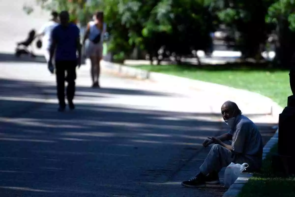 Un hombre en el parque del Retiro con mascarilla y sentado a la sombra