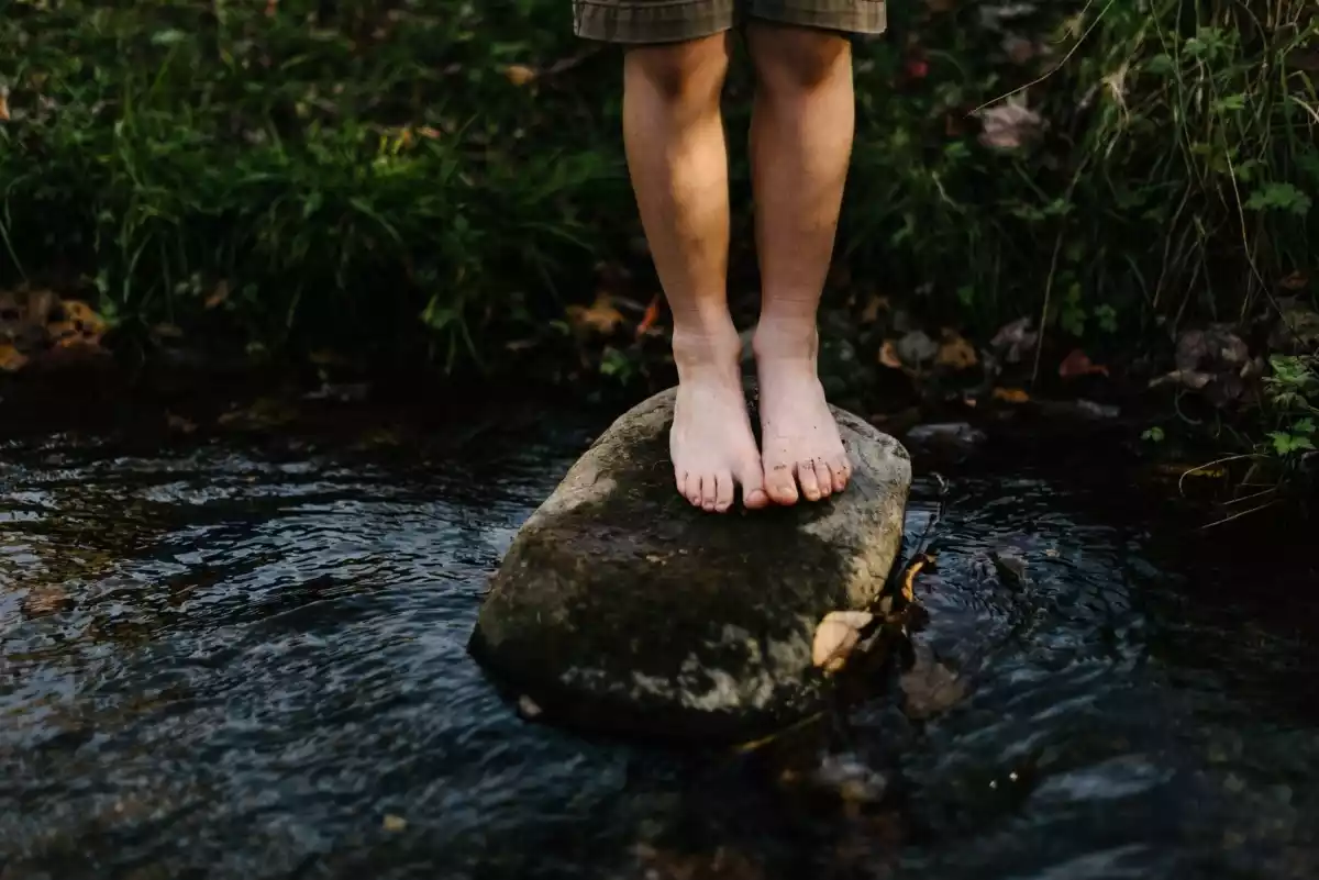 Una persona delcalza sobre una piedra en un río