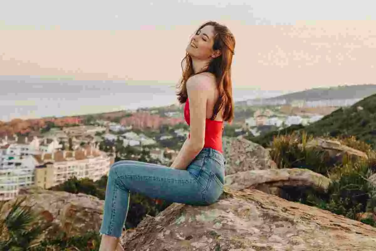 Chica joven sentada sobre unas rocas, sonriendo