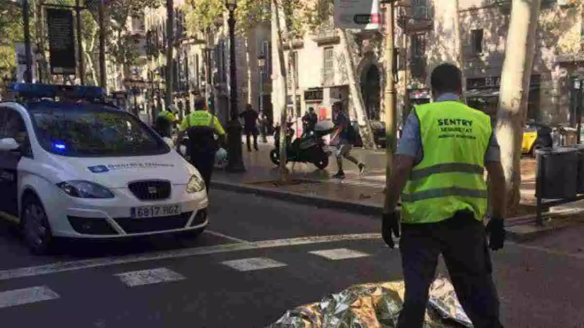 Imagen de un coche de policia en las Ramblas de Barcelona con una víctima de los atentados delante