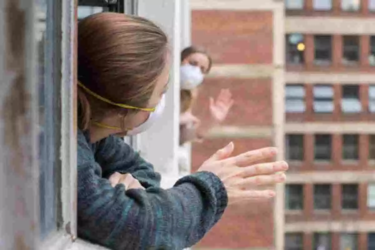 Dos mujeres con mascarilla saludándose desde las ventanas de un edificio