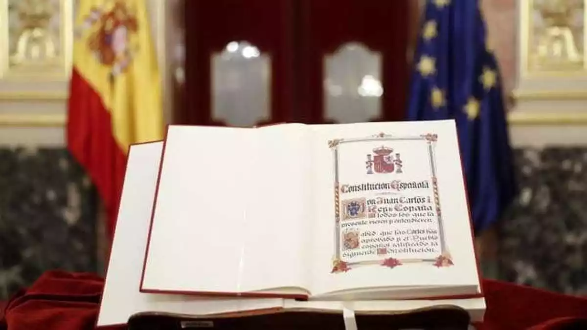 Imagen de un ejemplar de la Constitución Española con banderas al fondo