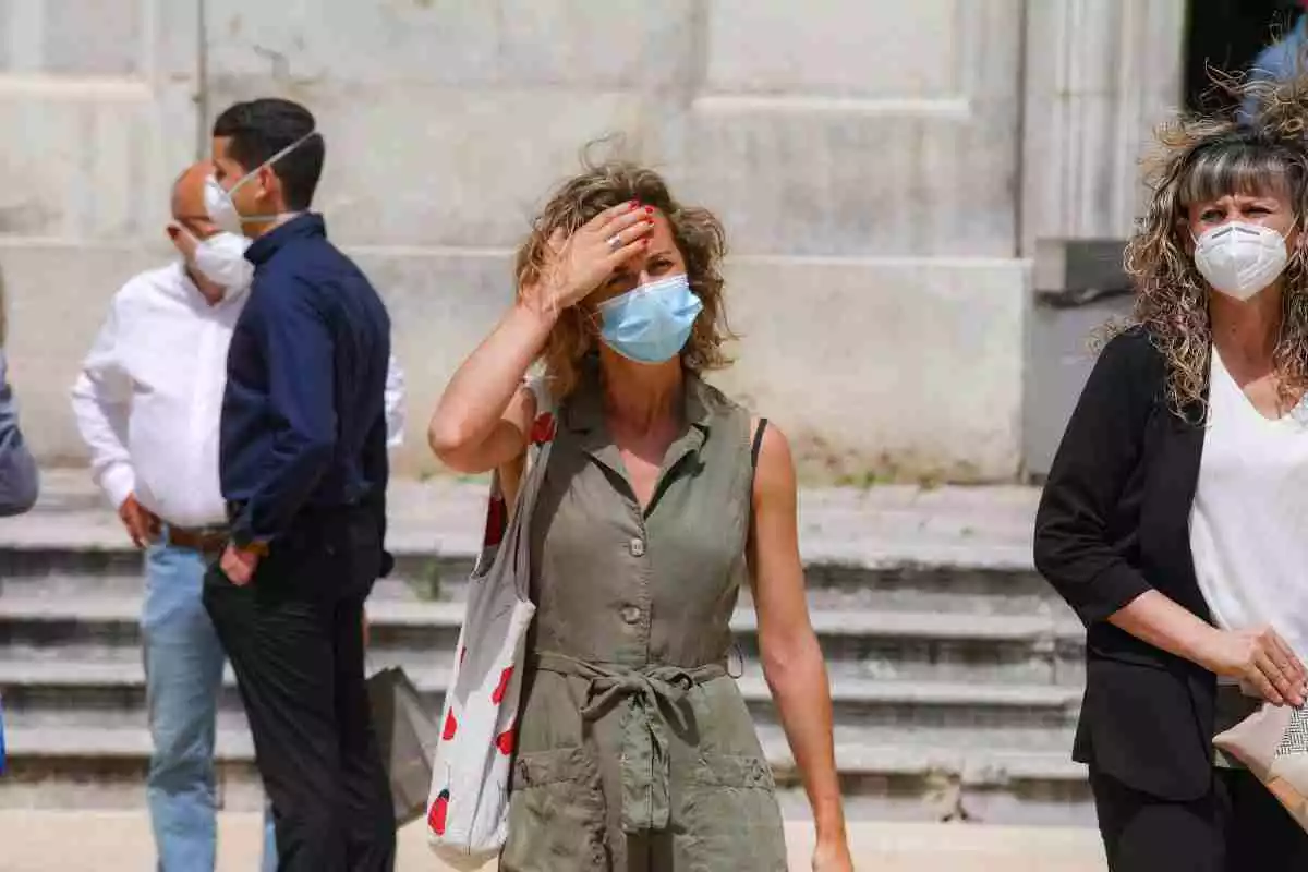 Una mujer se toca la frente por el calor con mascarilla higiénica