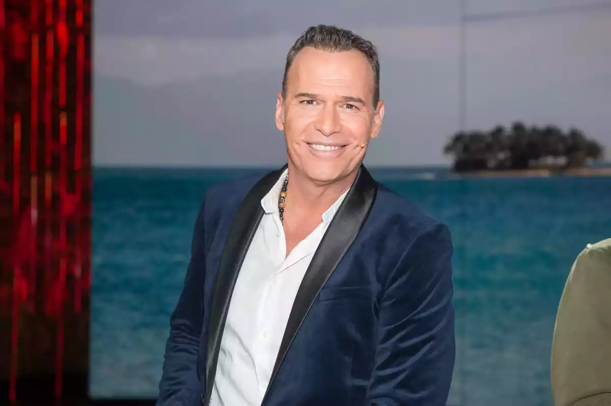 Carlos Lozano sonriente con una imagen del mar de fondo en un plató de televisión