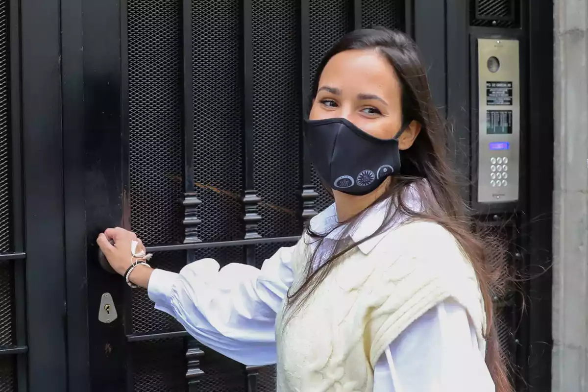 Carolina Monje sonriendo frente a una puerta negra con su mano apoyada en el pomo para abrilra