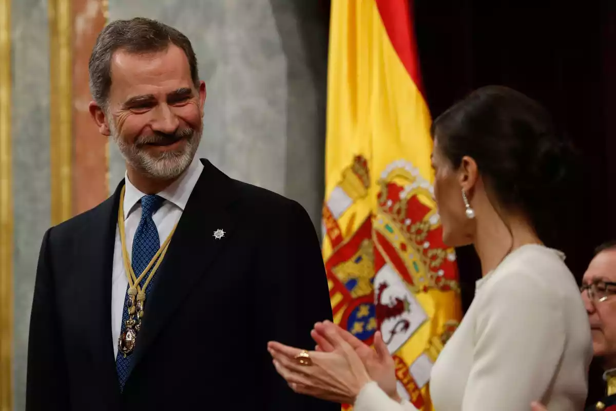 El Rey Felipe VI en un acto público con su mujer, la Reina Letizia, con la bandera de España de fondo