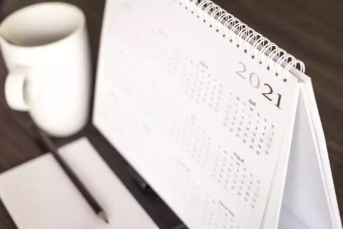 Imagen de un calendario de 2021 sobre una mesa junto a un lápiz, papel y una taza