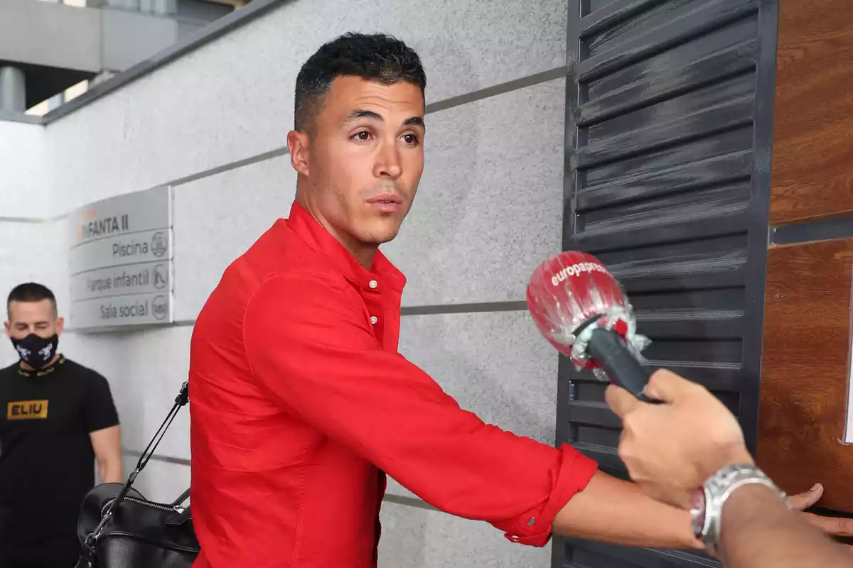 Kiko Jiménez con camisa roja con una pared y puerta al fondo atendiendo a la prensa