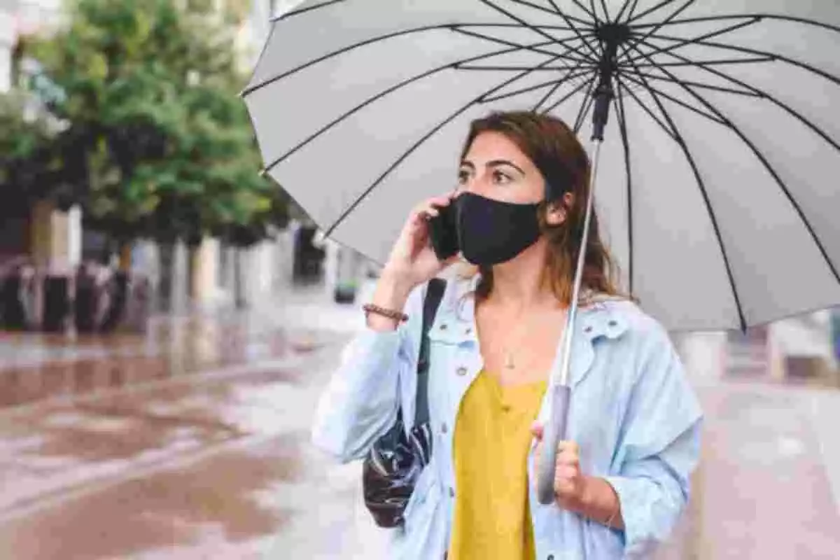Mujer con mascarilla y paraguas hablando por teléfono en la calle bajo la lluvia