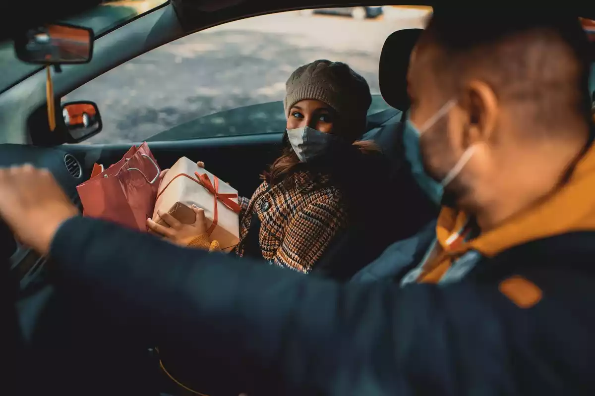 Una chica con varios regalos y mascarilla dentro del coche acompañada por otro hombre