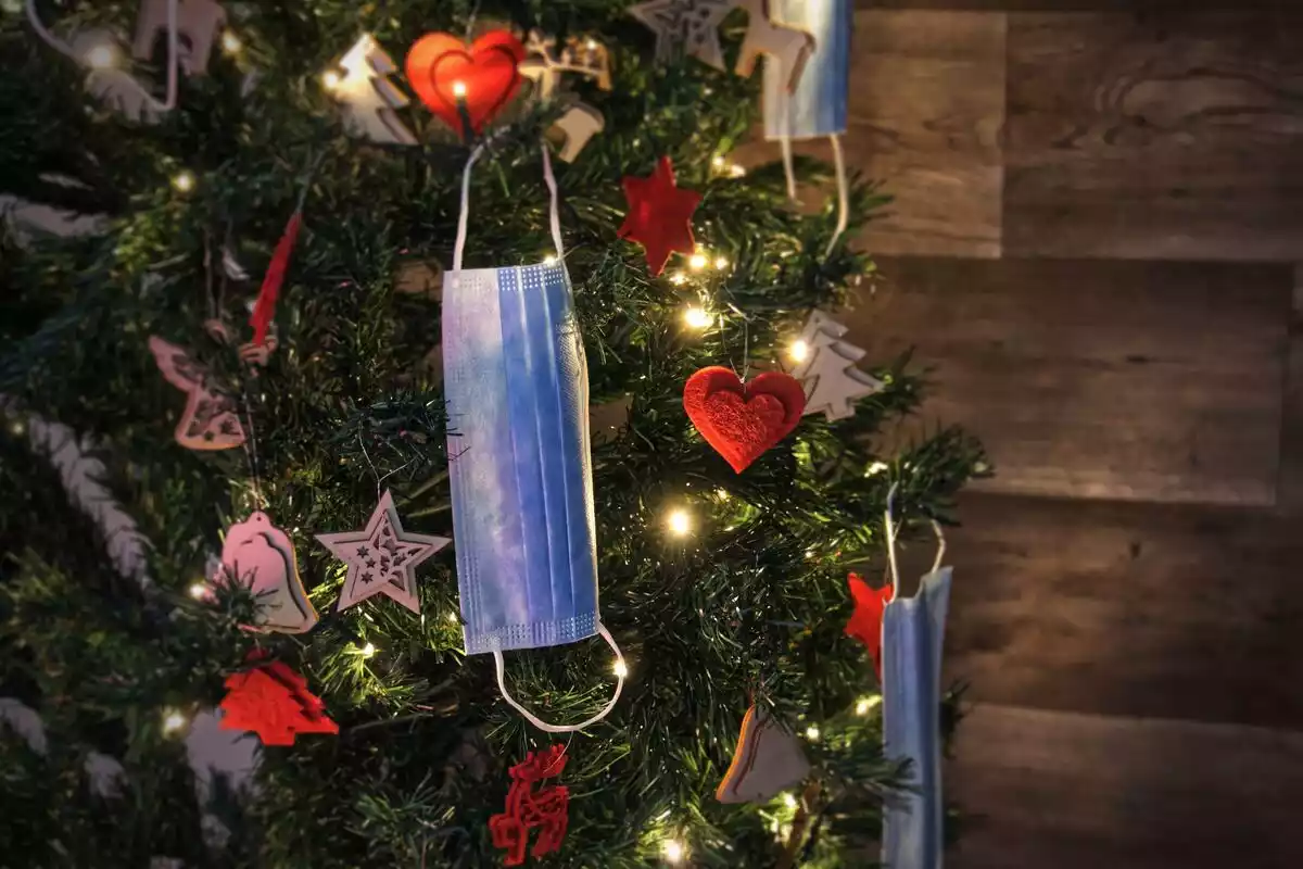 Una mascarilla colgando de un árbol de Navidad decorado con luces y estrellas