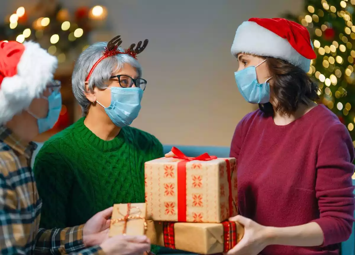 Varias personas con ropas navideñas y mascarilla sostienen regalos de Navidad