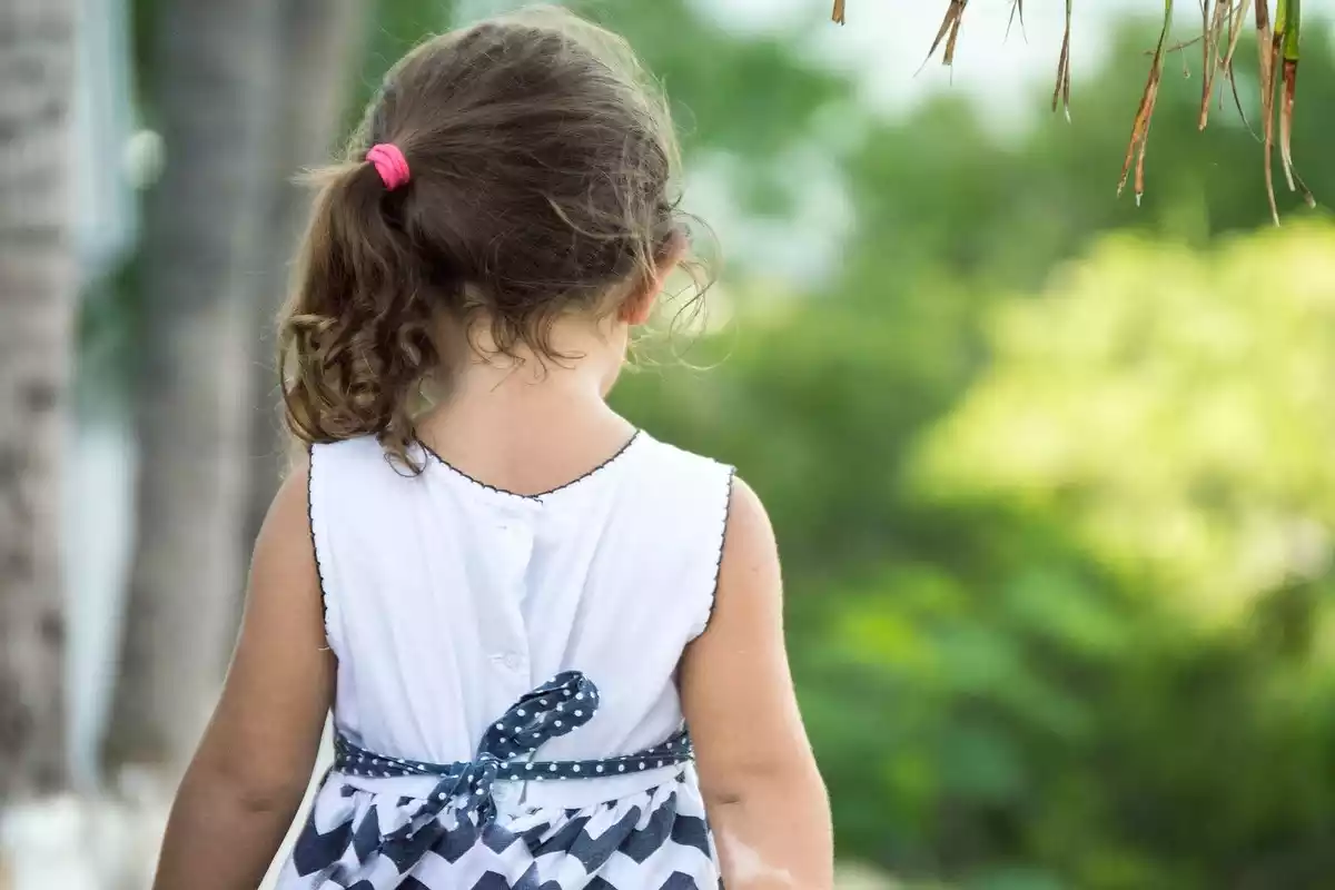 Imagen de archivo de una niña con un vestido de verano de espaldas en la naturaleza