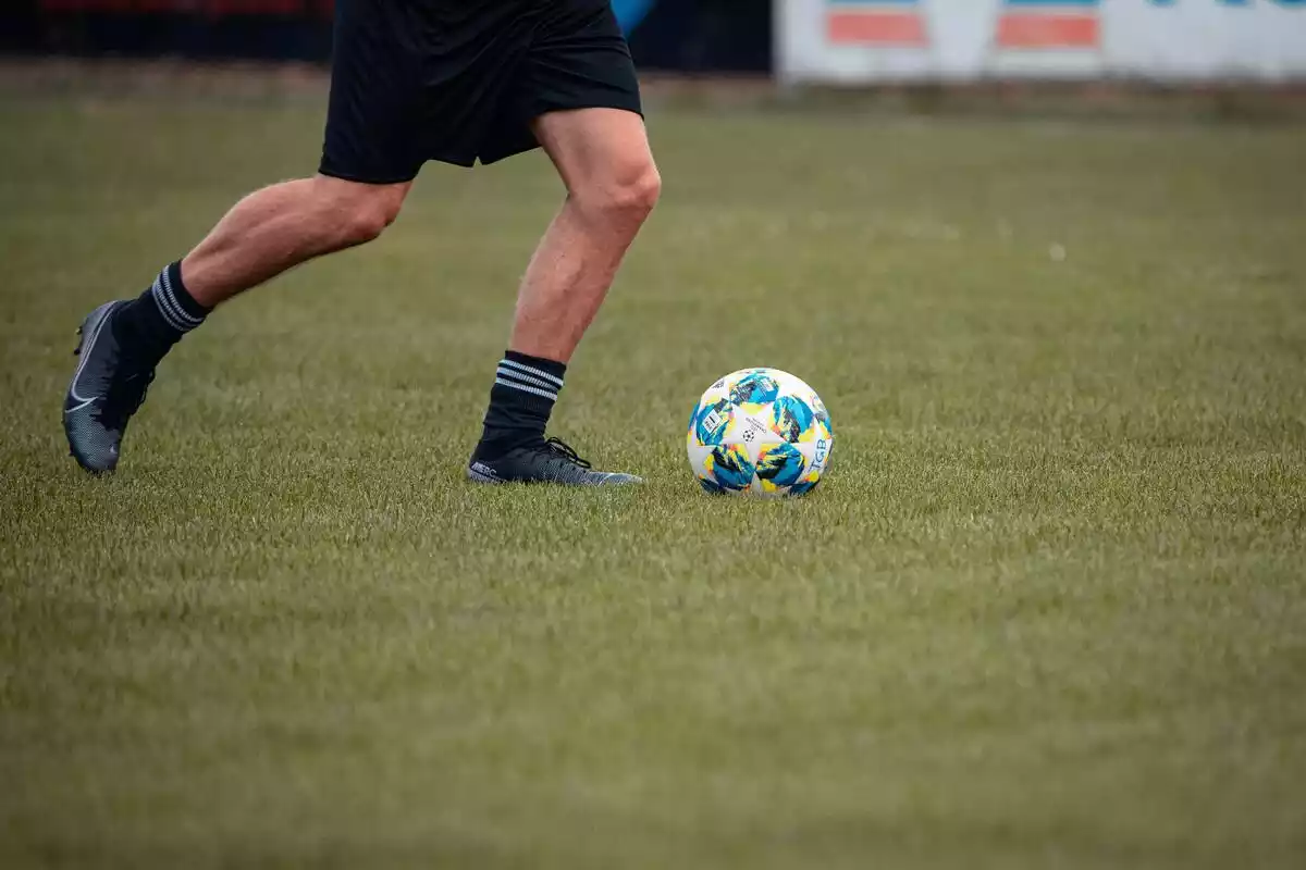 piernas de jugador de fútbol cerca de pelota en campo de césped