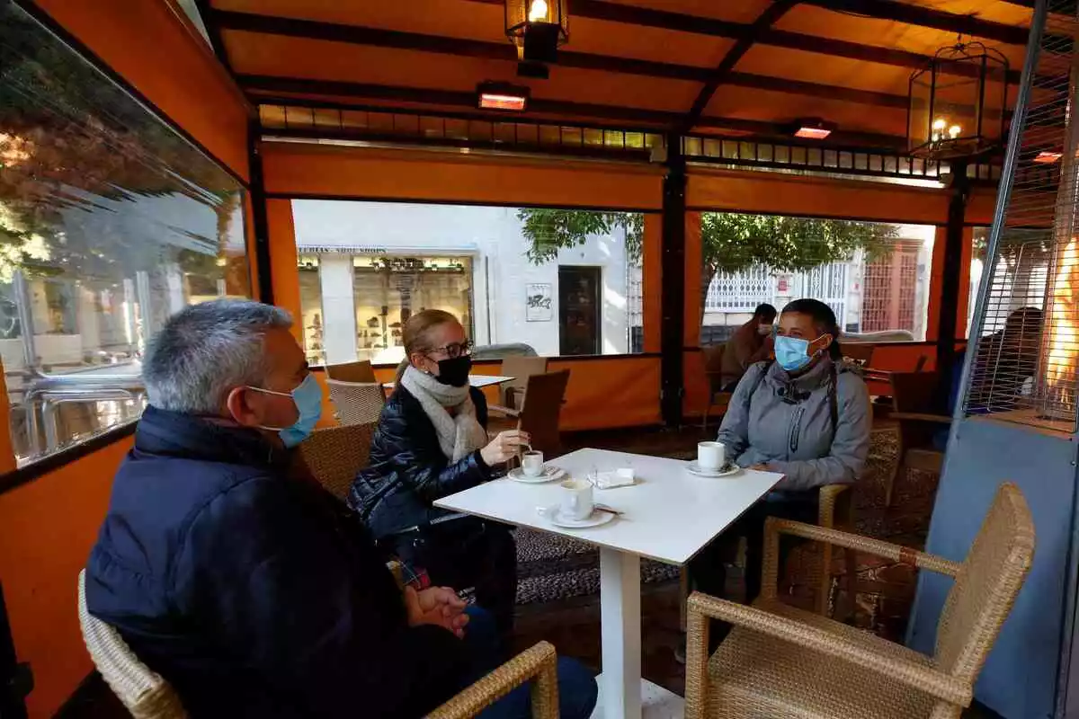Tres personas en una mesa en una terraza cubierta de un bar