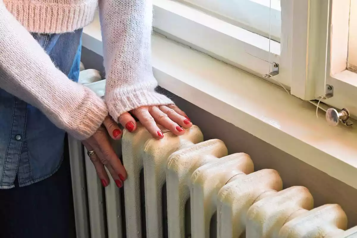 Una mujer calienta sus manos sobre un radiadior