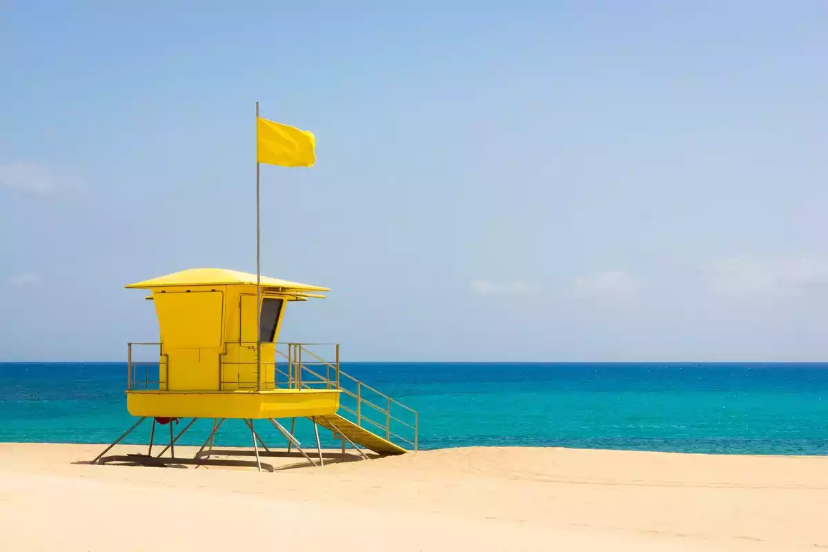 Fotografía de un puesto de color amarillo en la playa con una bandera del mismo color
