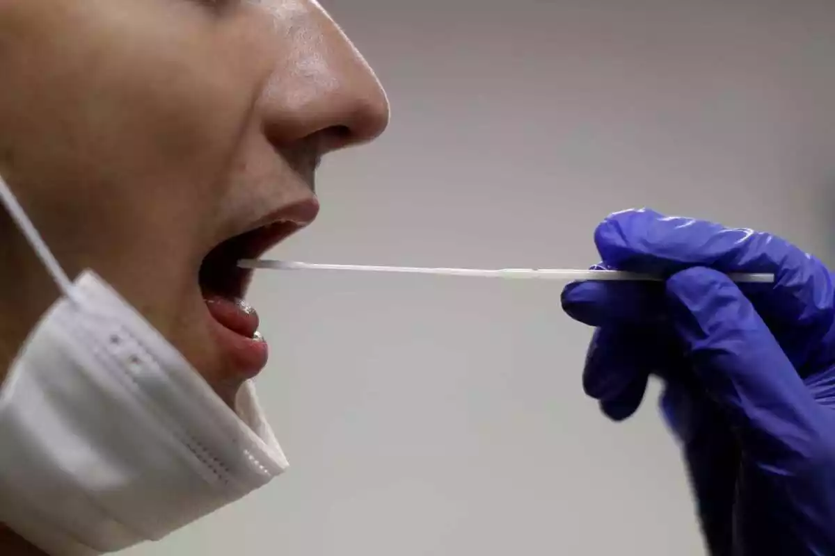 Sanitario introduciendo un hisopo a una persona en la boca para hacer un test covid