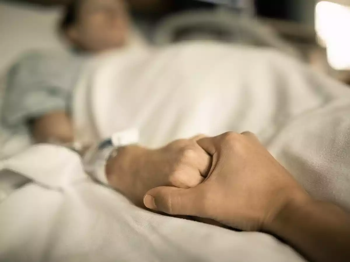 Un hombre sujeta la mano de una mujer en la cama del hospital