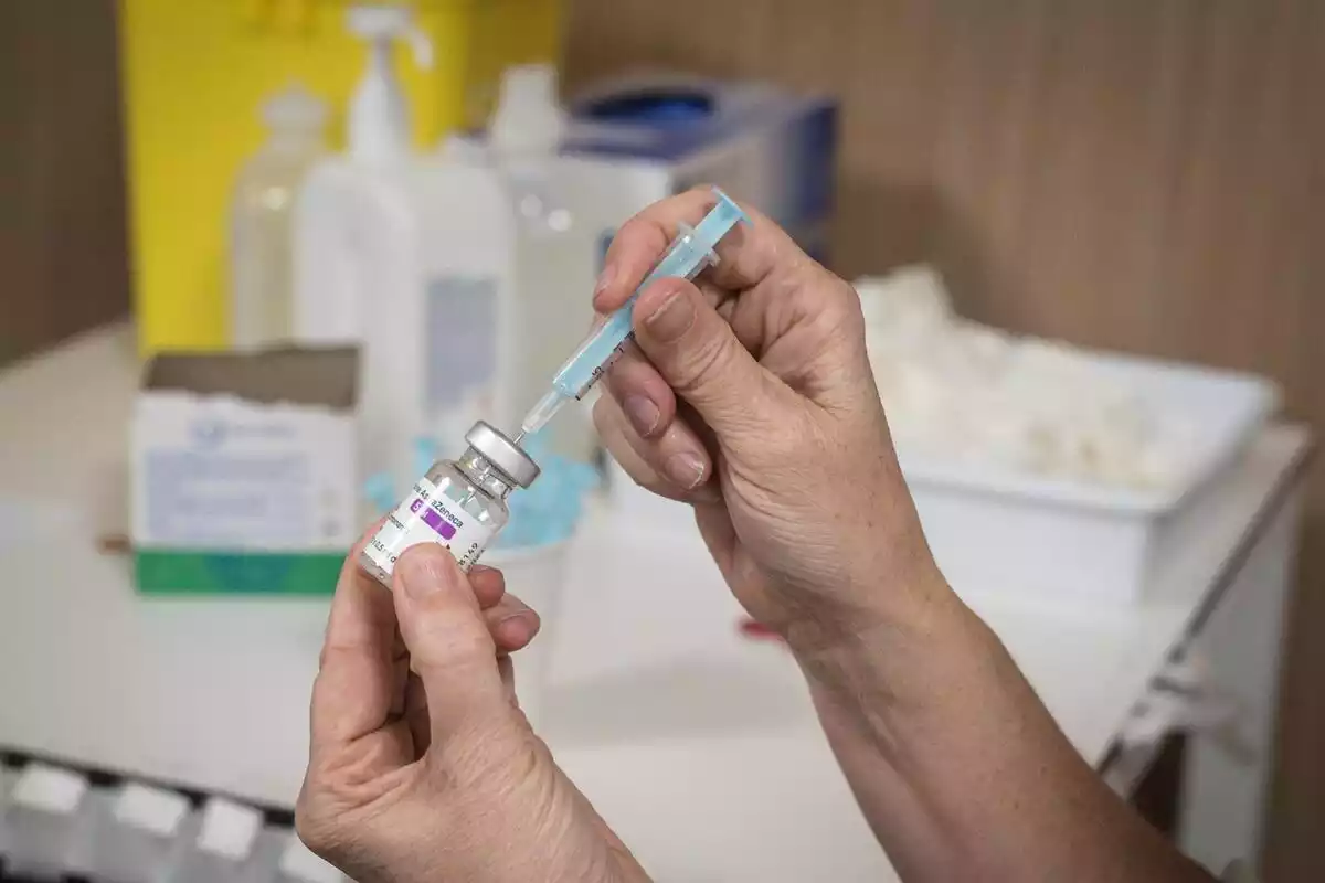 Un sanitario introduciendo una aguja en un bote de la vacuna de AstraZeneca