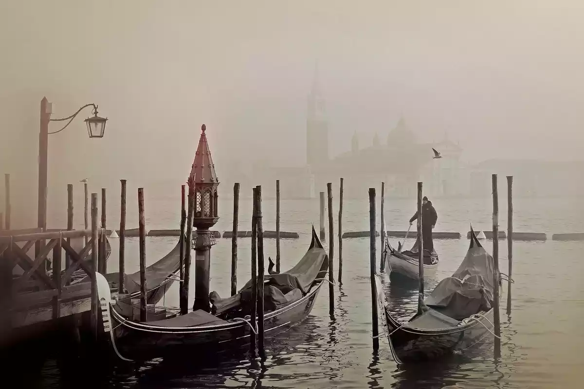 Unas góndolas en Venecia en un día con mucha niebla y un hombre paseando por detrás