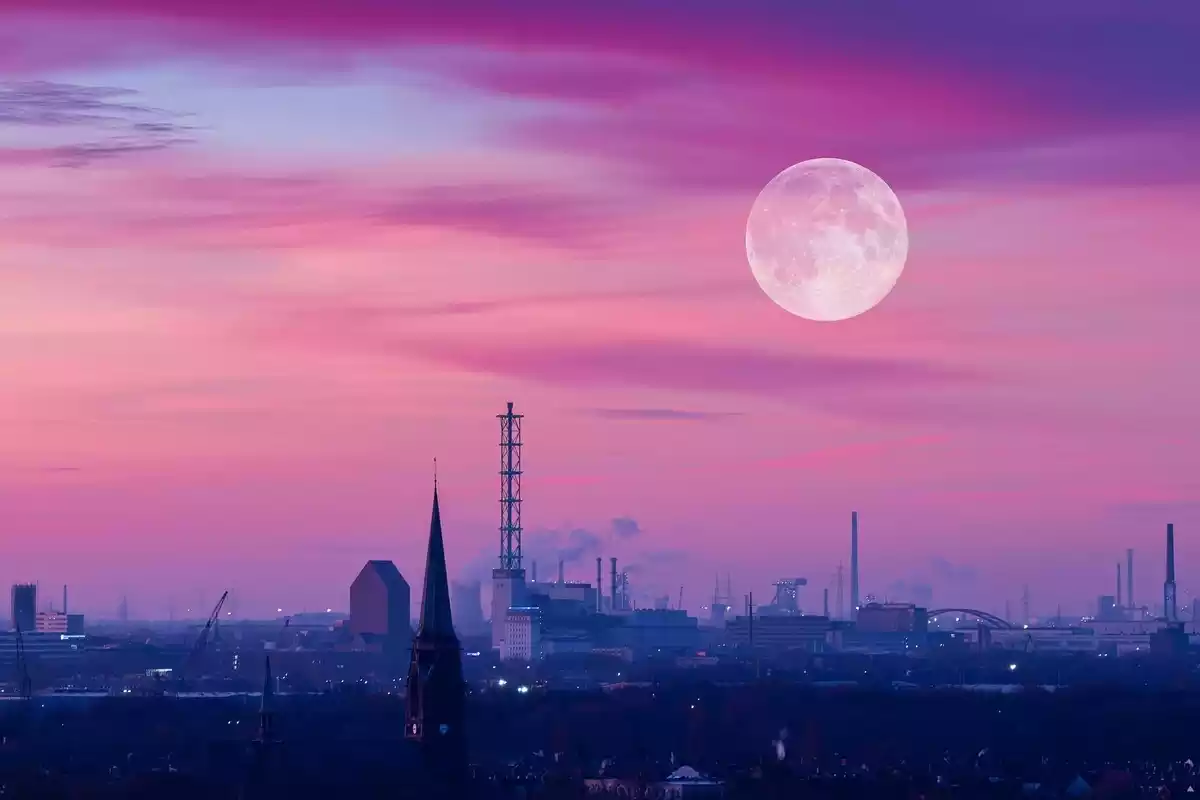 Luna llena con una tonalidad rosácea sobre una ciudad industrial