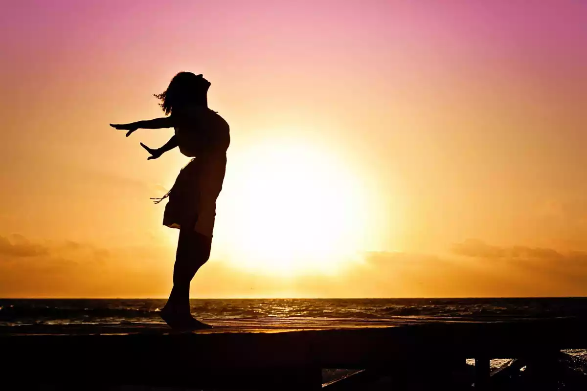 Silueta de una mujer con vestido delante de una puesta de sol en la playa