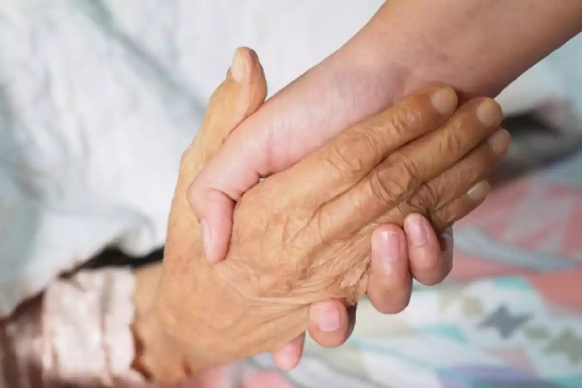 Una mano de una persona joven agarra la mano de una anciana