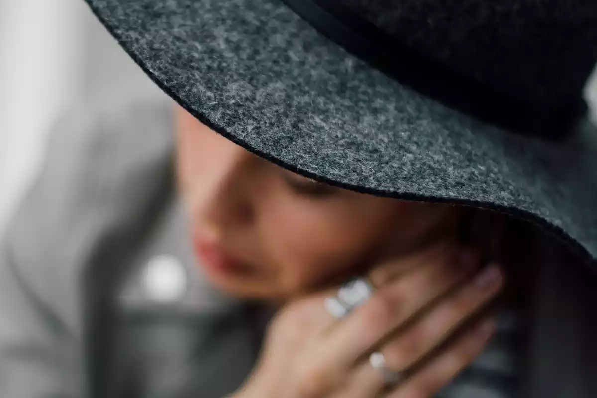 Una mujer con sombrero y unos anillos en la mano en un plano contrapicado